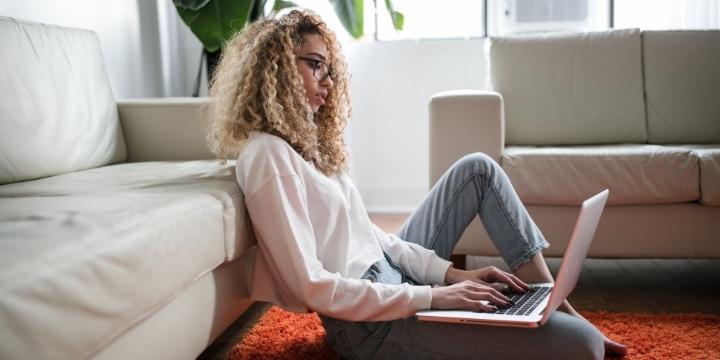 Mujer trabajando con portátil desde la alfombra de su salón (encuesta OCU sobre consumo Internet)