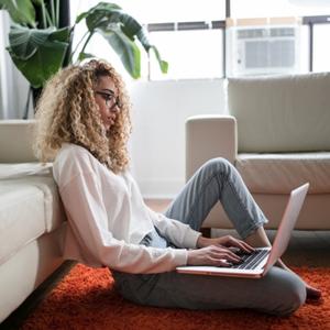 Mujer trabajando con portátil desde la alfombra de su salón (encuesta OCU sobre consumo Internet)